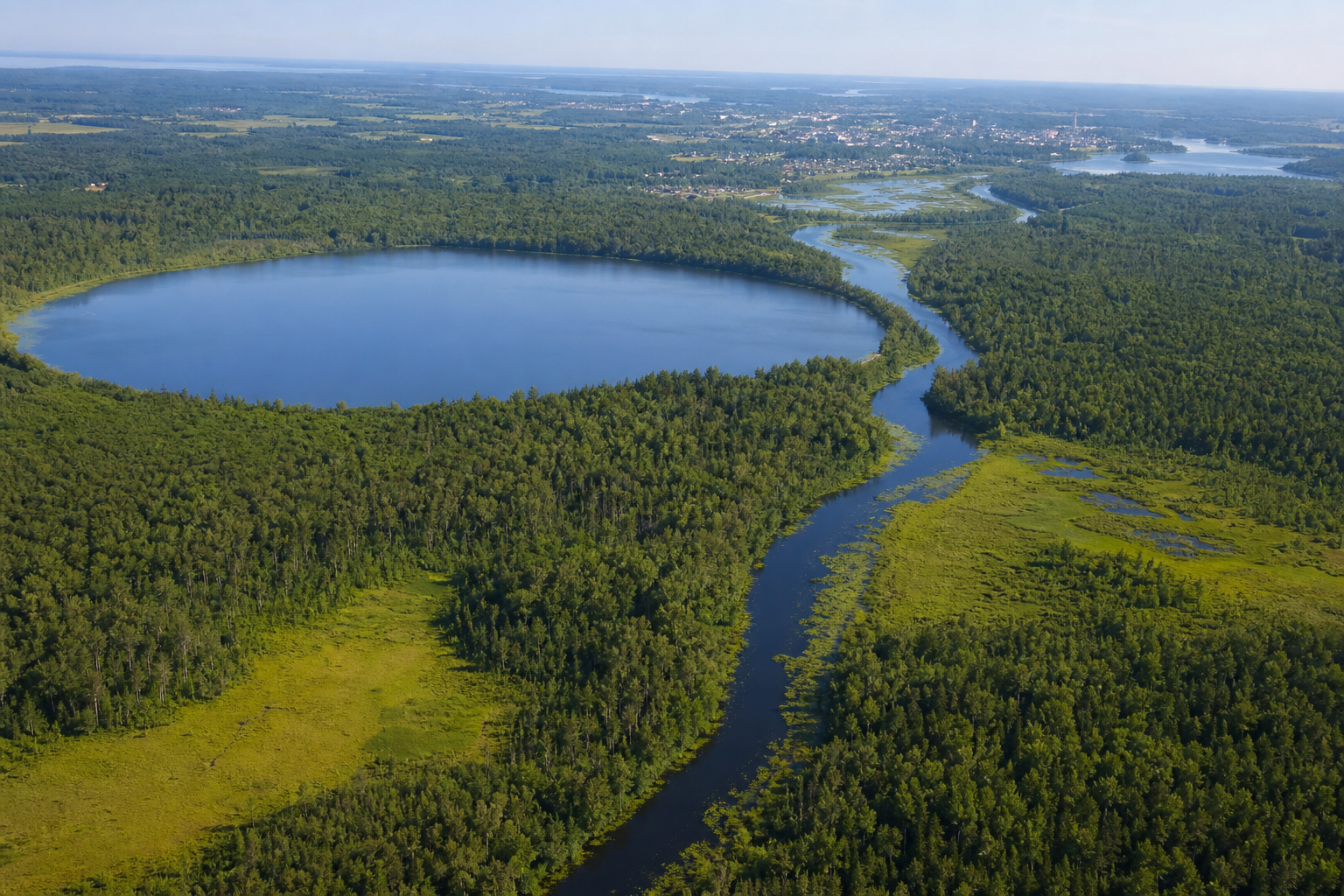 Vista aérea de un lago boscoso y un río sinuoso entre humedales del norte