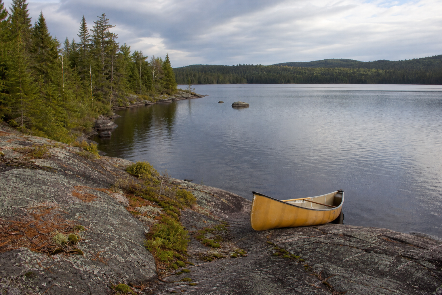 Empty canoe beside a clear boreal lake on a granite shoreline