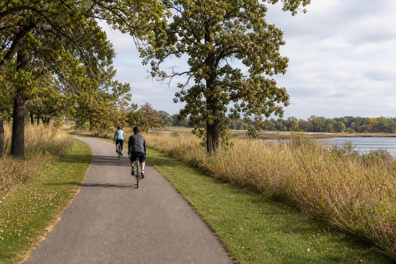 Two distant helmeted adults cycle on an illustrative paved trail through oak savanna beside a southern Minnesota wetland