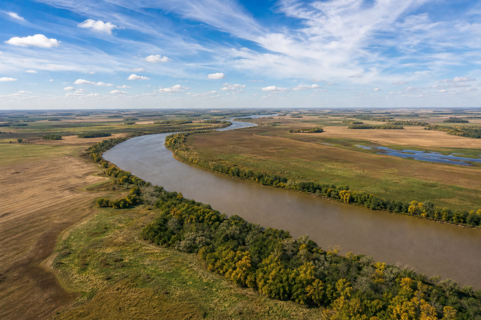 High view of a winding river through flat prairie fields and wetlands