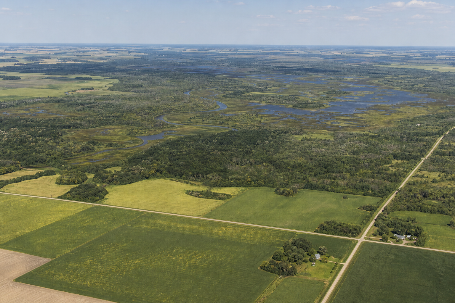 Elevated view of farm fields meeting an expansive wetland and winding river corridor
