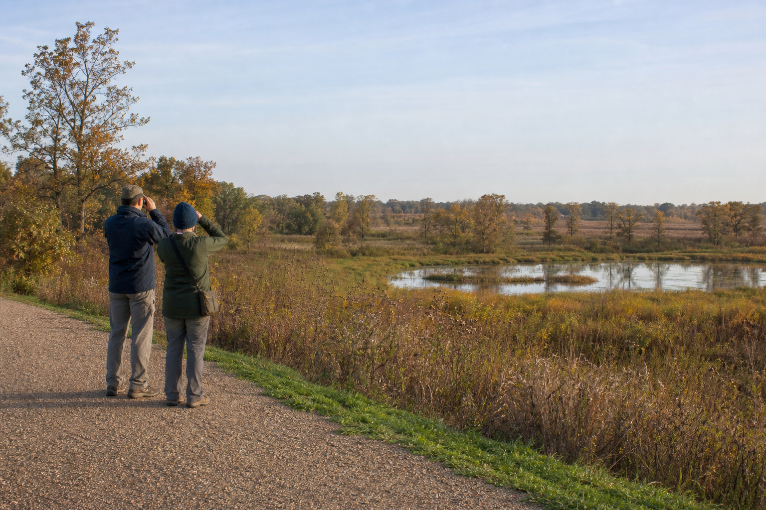 Two birdwatchers stand on an accessible gravel trail above prairie, oak savanna and wetland