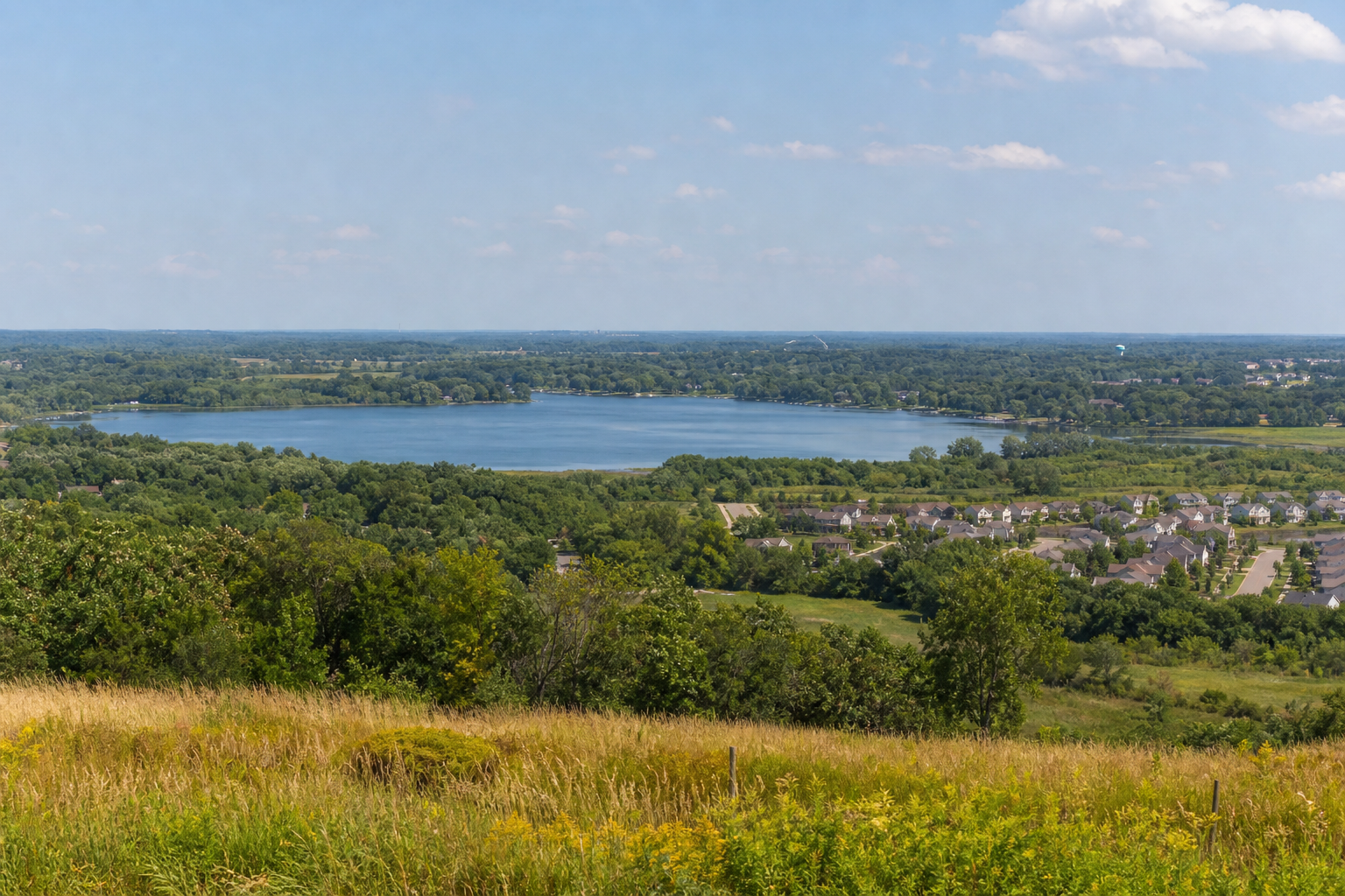 Elevated view across prairie and oak woods to an east-metro lake and nearby neighborhood